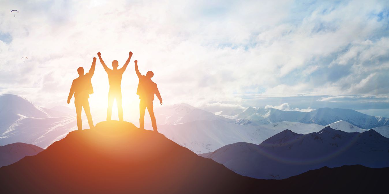 Erfolgreiche Führungskräfte aud der Bergspitze bei Sonnenaufgang